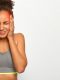horizontal shot of dissatisfied curly haired woman touches both temples suffers from migraine wears sports bra closes eyes from bad feelings isolated on white wall
